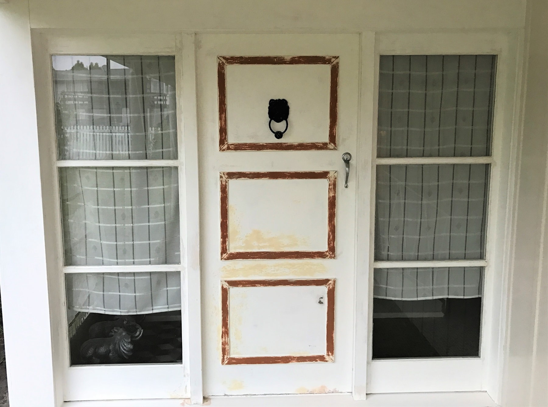 An entry door with cream paint flaking away from the timber panels and frame.
