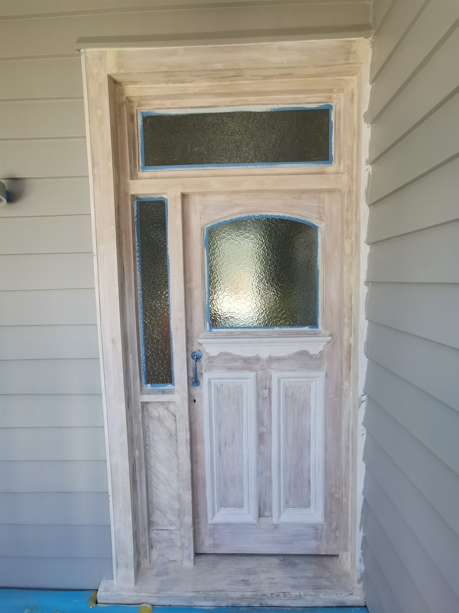 A villa front door sanded back to bare patchy timber, ready for paint.