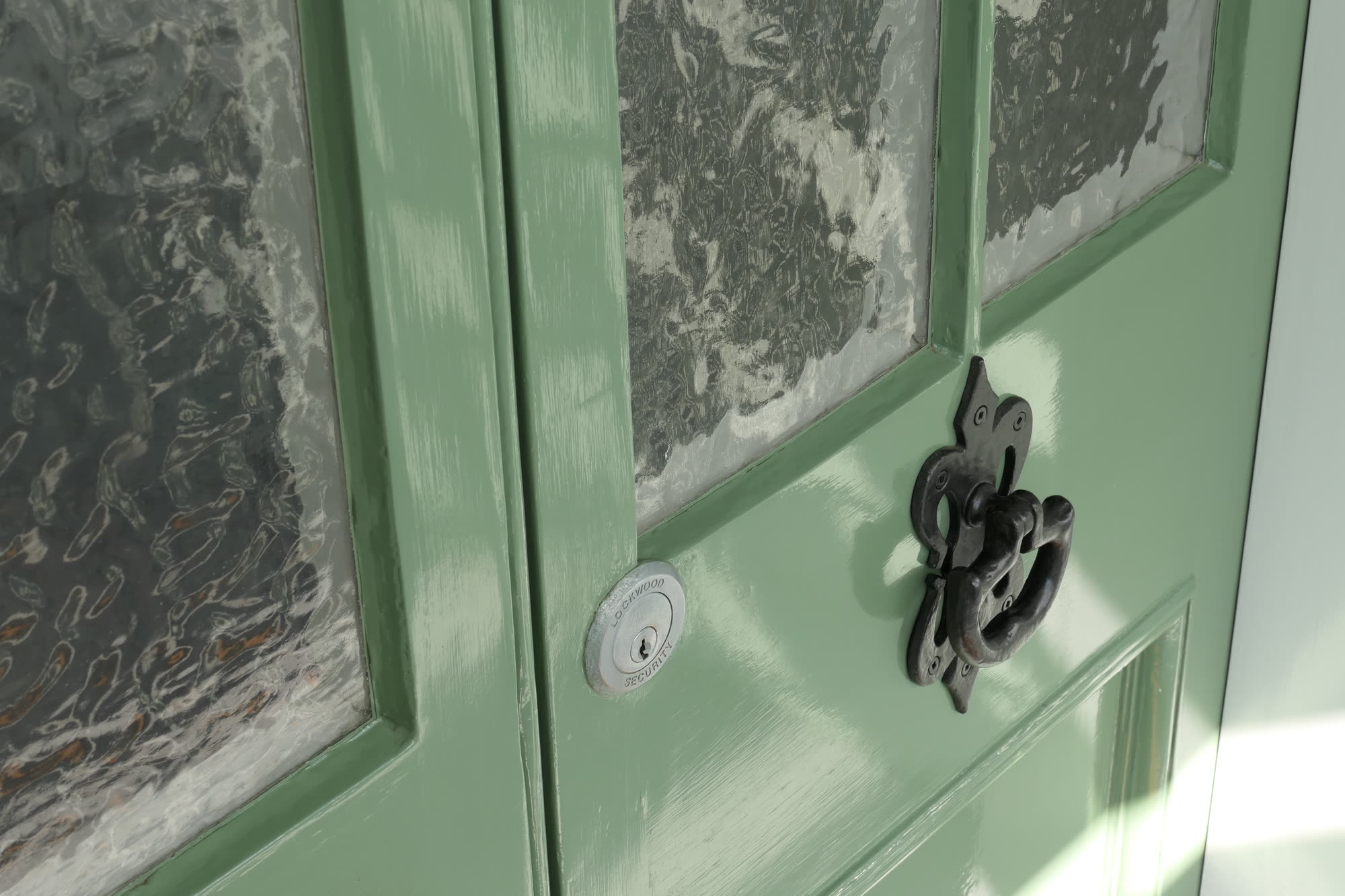 Close detail of a green front door, its cast-iron knocker and reeded glass panels lit by raking sun.