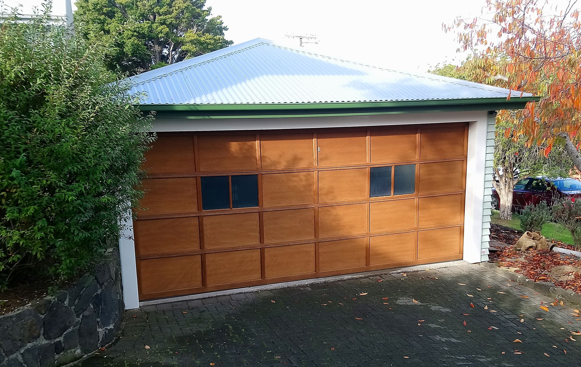 The same timber-panelled garage door finished in a warm golden tone, under a blue-grey roof.
