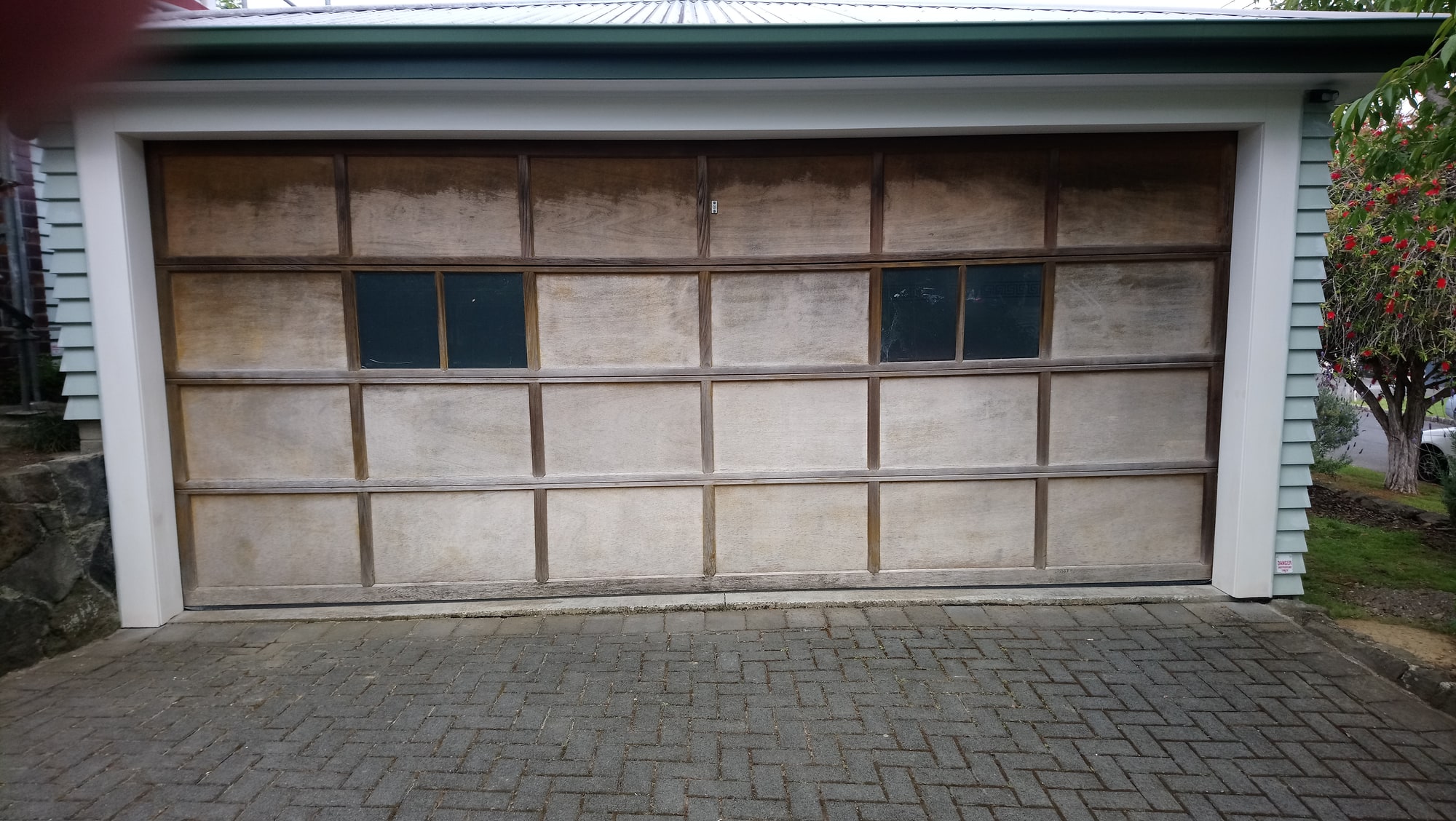A weathered timber garage door, its finish bleached and worn, set in a white surround.