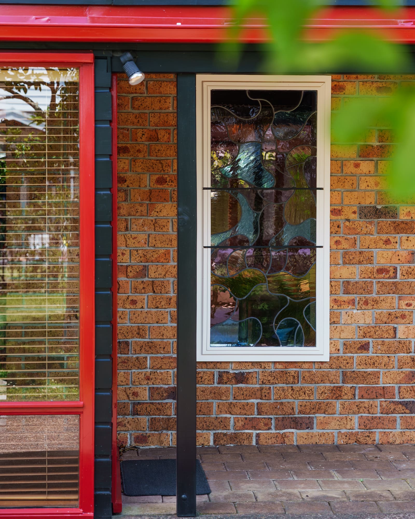 The entry door in white and red, beside a leadlight window and brick wall.