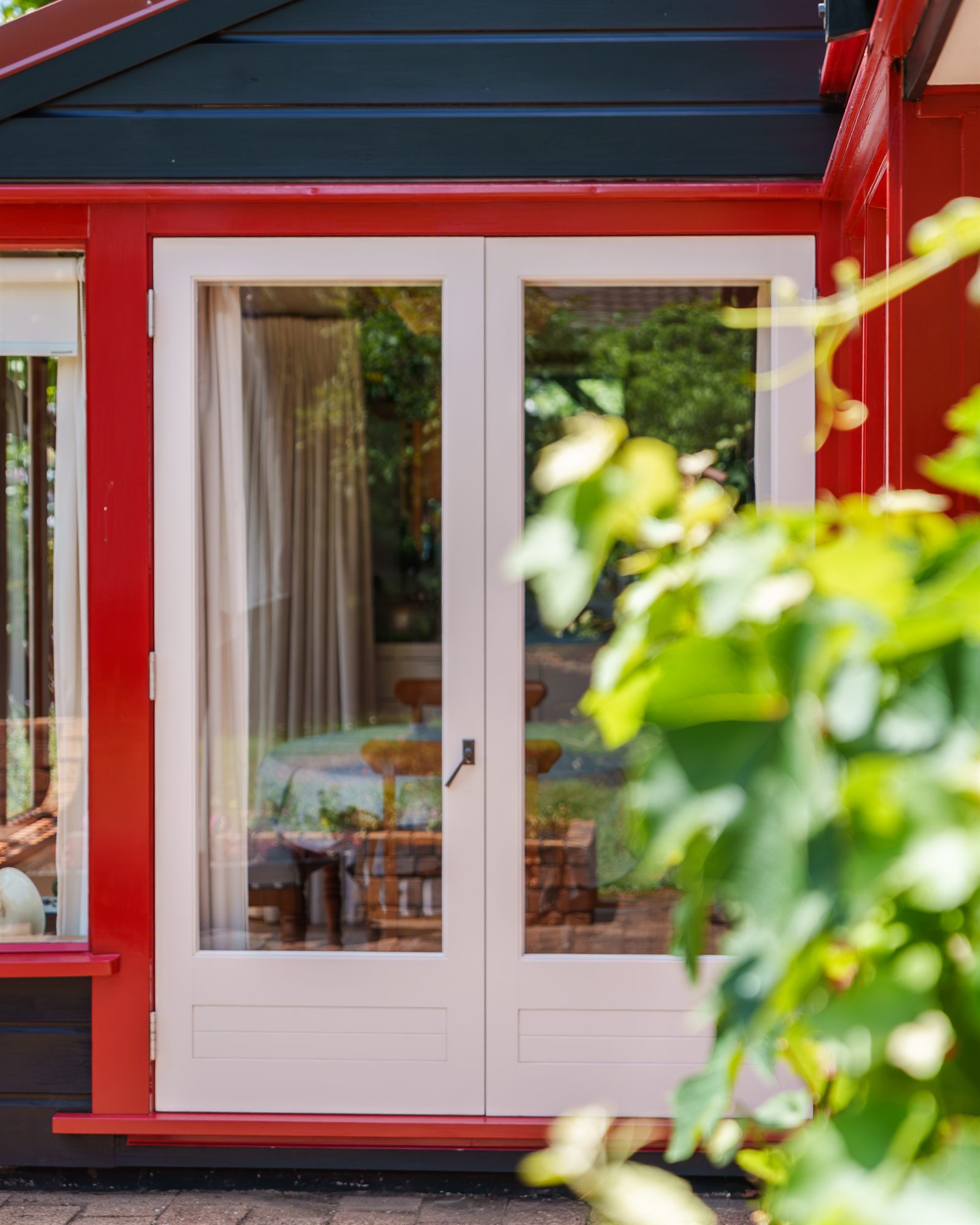 Cream french doors in a red-painted frame under a black soffit, seen past a grapevine.