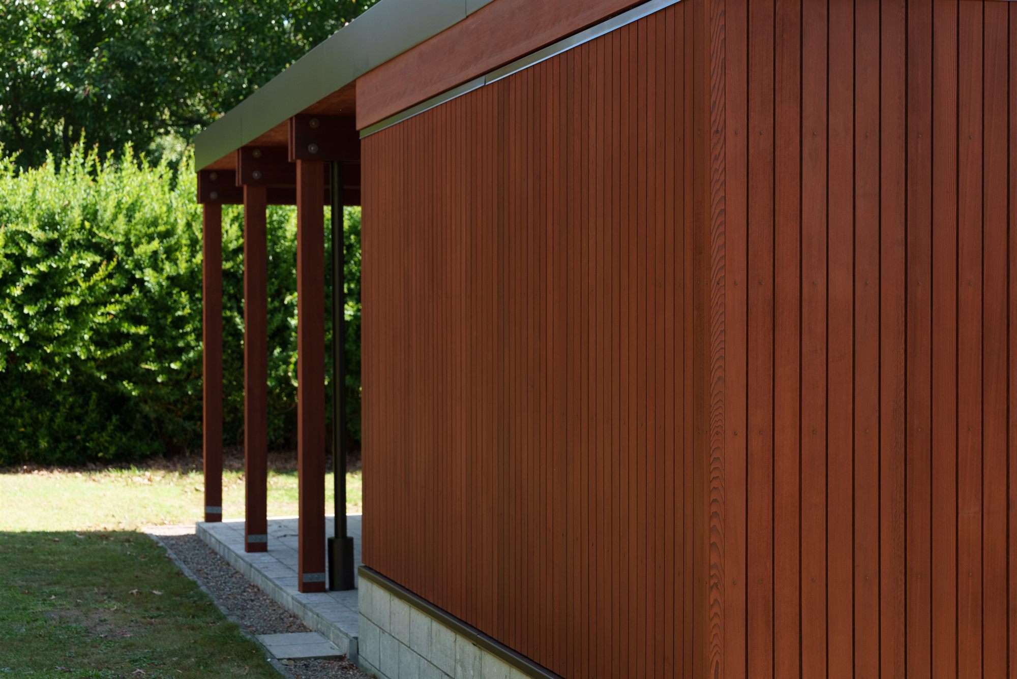 The corner of the cedar-clad pavilion in full sun, vertical boards running past a pale stone base.
