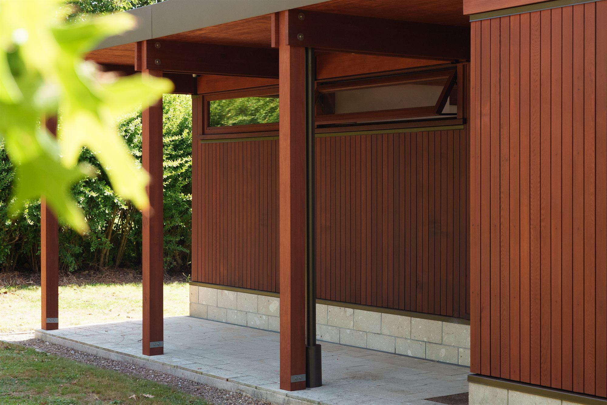 Cedar posts and vertical board cladding under the pavilion’s deep eave, an awning window propped open above.