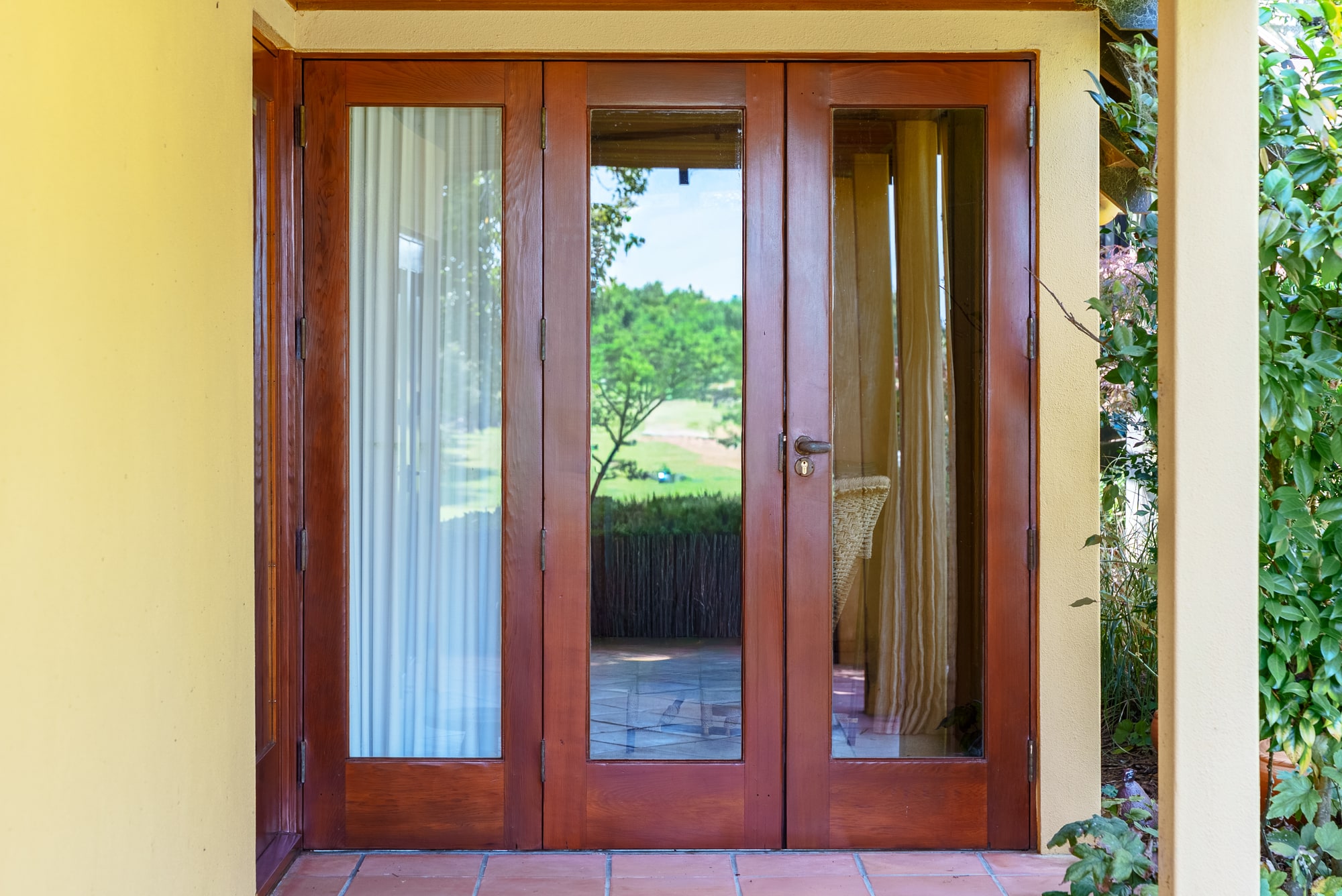 Varnished french doors in a cream rendered wall, opening onto a lawn.