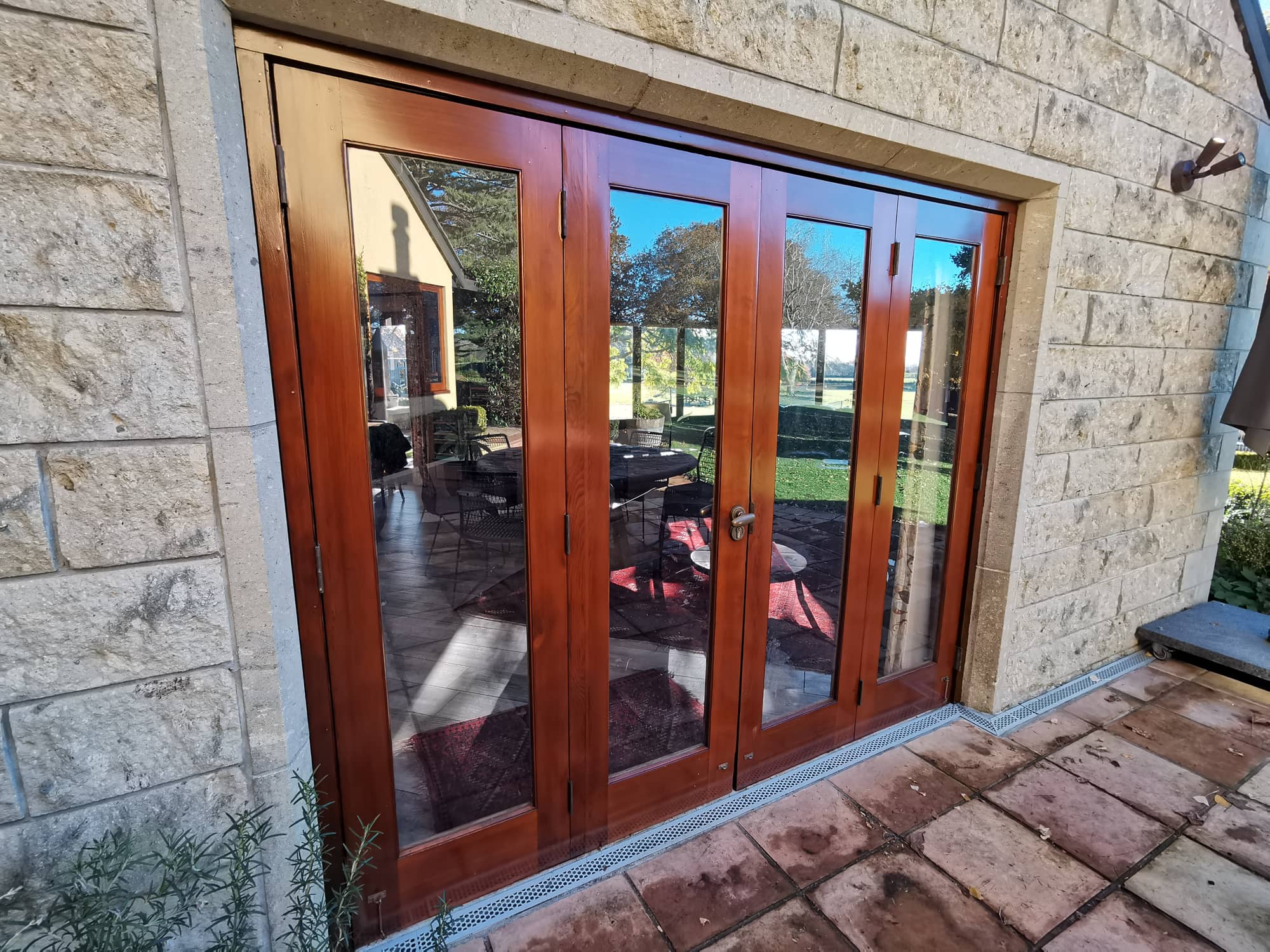 Varnished french doors set into a pale stone wall.