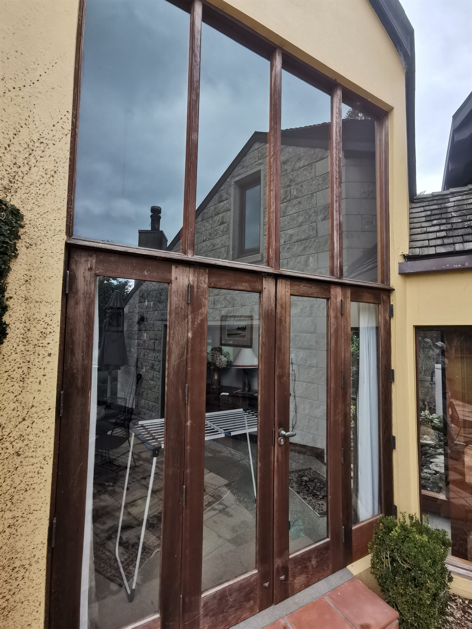 Tall gable glazing and doors with the finish worn back to dull, greyed timber.