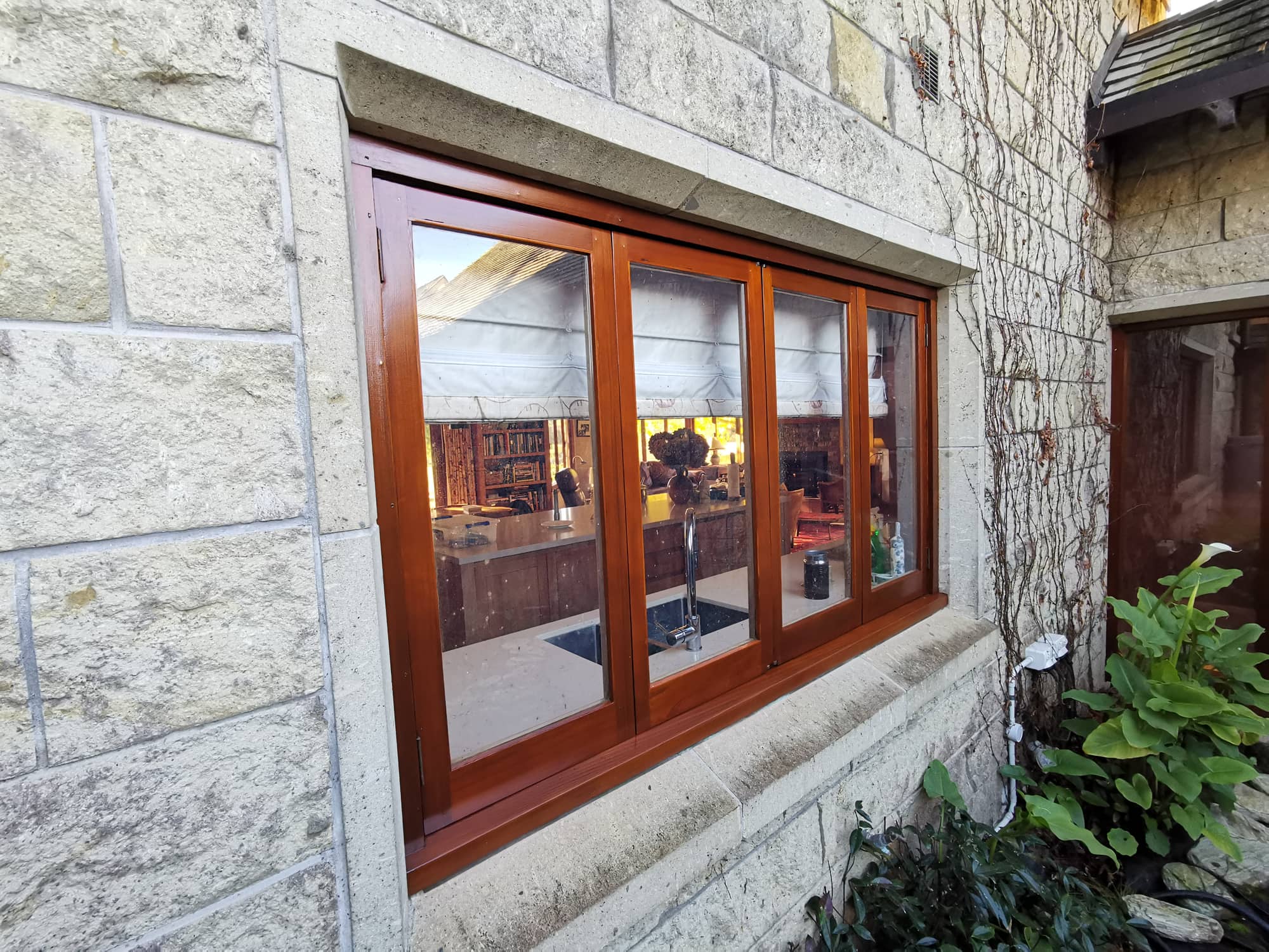 A varnished window in a stone wall framed by ivy.