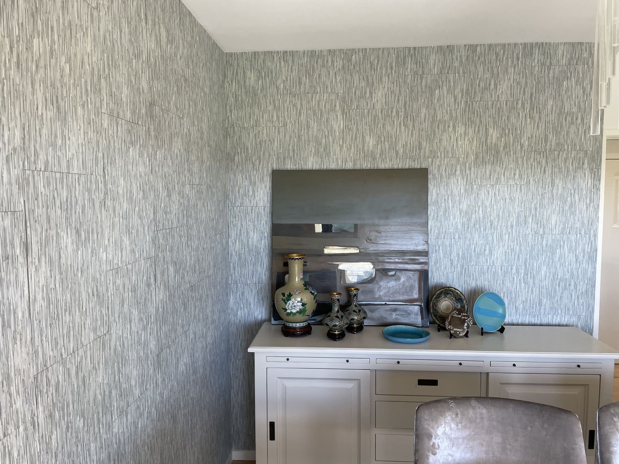 Silver textured wallcovering behind a white sideboard styled with ceramics.
